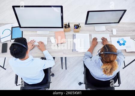Overhead view of two unknown business people working on computers on a desk in a office. Two colleagues wearing headsets working in a call center Stock Photo