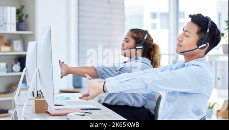 Some calls just make you question your choice in career. Shot of a young asian man and hispanic woman stretching while using a headset and computer in Stock Photo