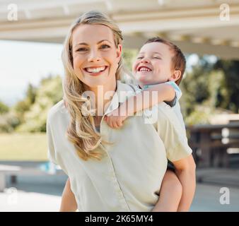 Happy single mother giving her little son a piggyback ride outside in a garden. Smiling caucasian single parent bonding with her adorable child in the Stock Photo