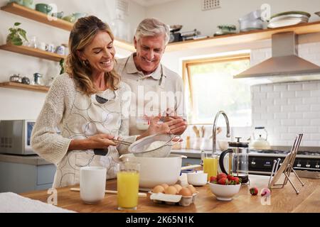 Elderly, couple and in kitchen while cooking, baking and happy together in funny moment. Senior man, woman and retirement smile in home, bonding and Stock Photo