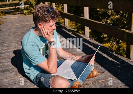 A frustrated entrepreneur working with a laptop on a wooden bridge in a park in the sunshine Stock Photo