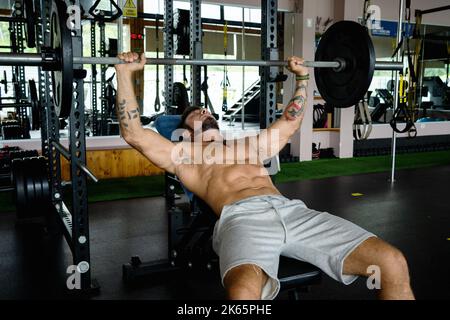 Strong man lying in a bench doing bench press exercises in a gym Stock Photo