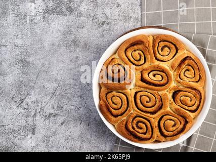 Cinnamon rolls or cinnabon, homemade sweet traditional dessert buns in a white baking dish on a dark grey background. Top view, flat lay Stock Photo