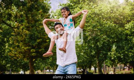Happy mixed race father and cute playful daughter having fun at the park outdoors with copyspace. Carefree man carrying cheerful girl on shoulders for Stock Photo