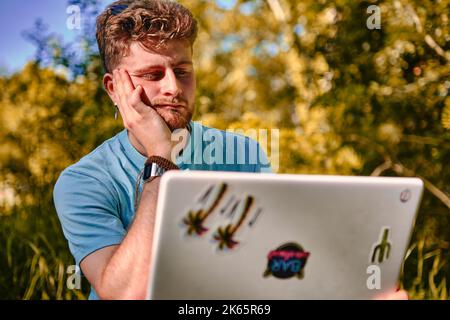 A young guy working outdoors on his laptop with a serious face with his hand under his chin Stock Photo