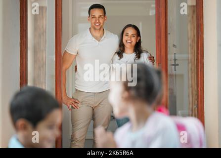 Parents standing at their front door and seeing off school children. Caring parents watching their son and daughter leaving home for school. Mom and Stock Photo
