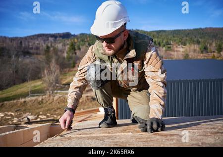 Man worker building wooden frame house. Carpenter using tape measure for measuring OSB sheet on rooftop. Carpentry concept. Stock Photo