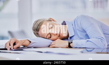 Tired young caucasian business woman sitting at desk and sleeping. Exhausted young female professional taking a nap lying her head on the table Stock Photo