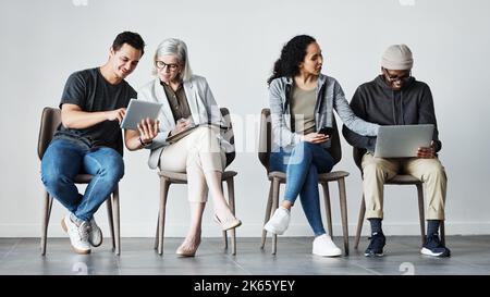 Businesspeople sitting in row using tech devices. Diverse businesspeople waiting for an interview, talking. Group of businesspeople collaborating Stock Photo