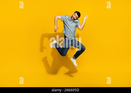 Full length portrait of satisfied glad young person jumping arms make moves isolated on yellow color background Stock Photo