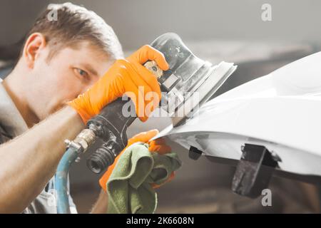 Auto mechanic grinds white car part after painting before polishing, close-up. Stock Photo