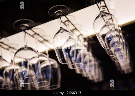 Empty wine glasses hanging upsidedown in bar interior. Stock Photo
