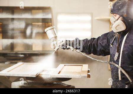 Close-up portrait of worker using spray gun and painting wood. Stock Photo
