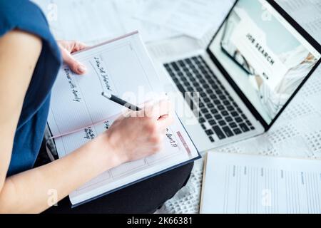 Job interview, Finding New Job. Young woman writing in Planner diary notes about job interview sitting near laptop on the bed at home Stock Photo