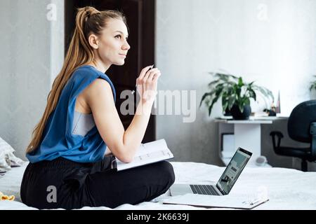 Job interview, Finding New Job. Young woman writing in Planner diary notes about job interview sitting near laptop on the bed at home Stock Photo