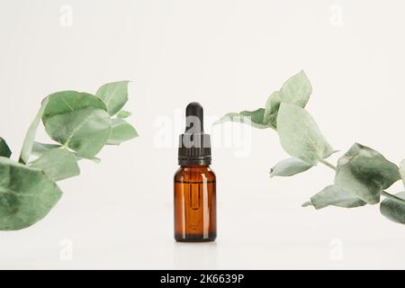 Glass dropper vial mockup decorated with plants on white. Stock Photo