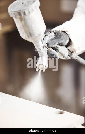 Vertical close-up of industrial worker using paint gun or spray gun for applying paint, airless spraying. Stock Photo