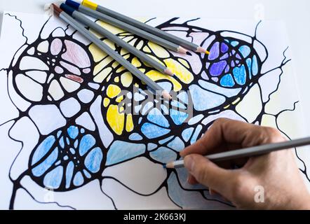 A woman draws a neurographic drawing on paper with color pencils. Neurographic art is an easy way to work with the subconscious mind through drawing. Stock Photo