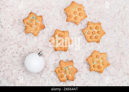 Top view of star shaped Christmas gingerbread cookies and decorative white ball on pieces of ice background. Festive Christmas and New Year background Stock Photo