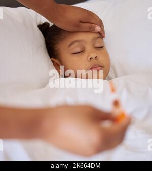 Sick little girl in bed while her mother uses a thermometer to check her temperature. Mixed race parent feeling daughters forehead. Hispanic child Stock Photo