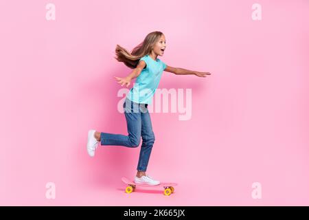 Full length photo of funky impressed little child dressed teal t-shirt riding skateboard empty space isolated pink color background Stock Photo