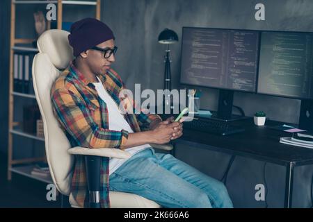Photo of cool happy guy dressed eyewear hat chatting twitter facebook telegram modern device indoors workstation workshop home Stock Photo