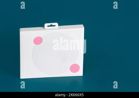 A blank white cardboard box with two small pink decorative circles around a large gray circle on a colorful blue studio background with copy space. St Stock Photo