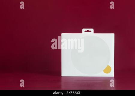 A white cardboard box with a large blank grey circle and a small gold one on a colorful red studio background and copy space. Storage, delivery, and s Stock Photo