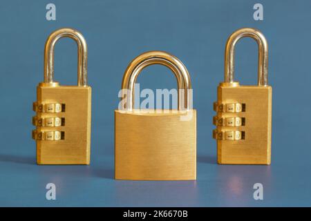 A golden square padlock escorted by two rectangular combination padlocks s in the background on a blue-painted study table. Leadership and security co Stock Photo