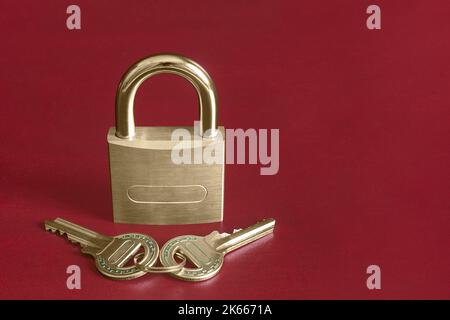 A closed gold padlock on a red studio background along with a pair of keys decorated with turquoise blue shapes and copy space. Security and trust con Stock Photo