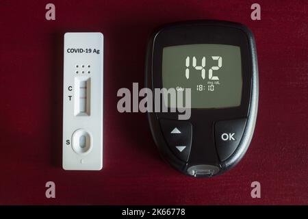 and-checking diabetes and high blood sugar with a digital blood pressure monitor and a rapid antigen test for Covid-19 with positive test results for Stock Photo