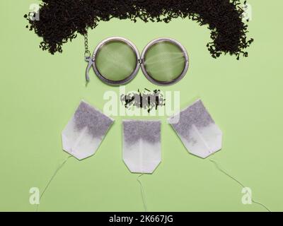 Three green tea bags, metal tea filter and heap of black tea on green background Stock Photo