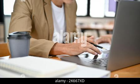Professional and smart Asian businessman or male boss working at his office desk, using laptop, typing on keyboard, doing his project on notebook comp Stock Photo