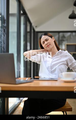 Exhausted, tired and overworked young Asian businesswoman or female office worker at her desk suffering from neck pain or office syndrome. Stock Photo