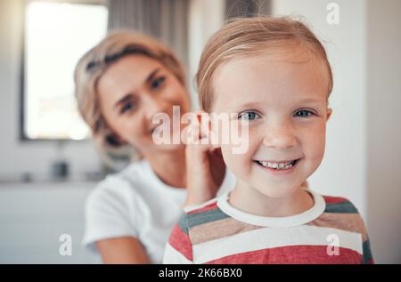 Loving mother brushing and tying little daughters hair. Adorable caucasian girl smiling while getting ready. Mom taking care of her daughter Stock Photo