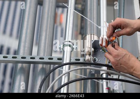 Electrical engineer connects wires to terminals in a junction box, close-up hands Stock Photo