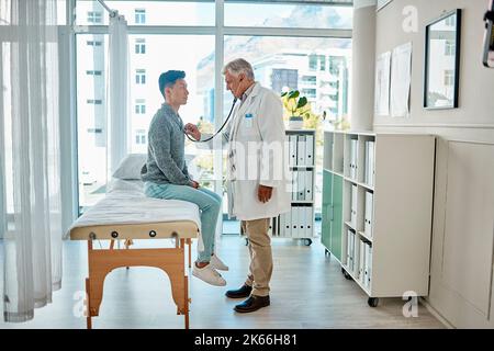 Caring caucasian man doctor using stethoscope to examine young male patients heart rate at consultation in hospital. Male physician taking care of his Stock Photo