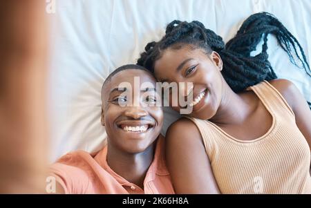 Closeup of happy african american couple taking a selfie while lying on their together. Young carefree couple relaxing in their bedroom and spending Stock Photo