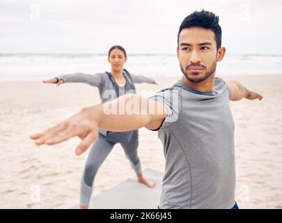 Boosting mood and mental clarity. a sporty young couple doing a warrior pose while practising yoga together on the beach. Stock Photo