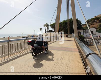 Man on a scooter crossing pedestrian bridge 'Puente de La Armada Española'. Fuengirola, Malaga provnce, Spain. Stock Photo