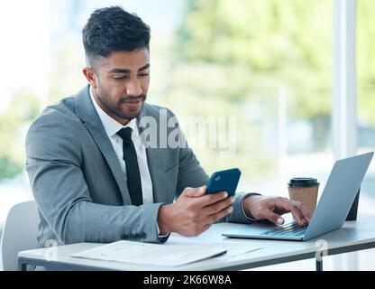 Another update just came in. a young businessman using a cellphone while working in an office. Stock Photo