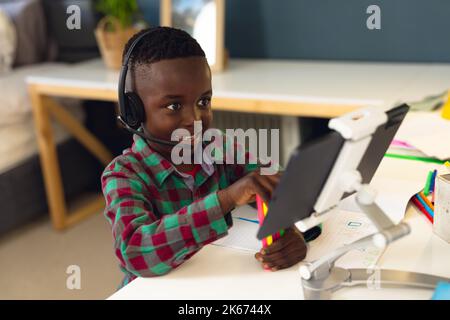 Smiling african american boy learning, using headphones and tablet at home Stock Photo