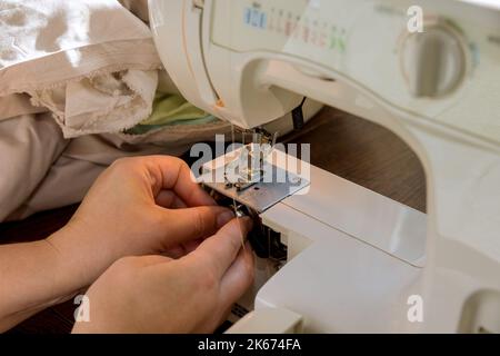 During sewing process seamstress places threads on metal spool in sewing machine Stock Photo