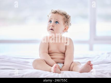 Put some clothes on me. an adorable baby boy sitting in his diaper at home. Stock Photo