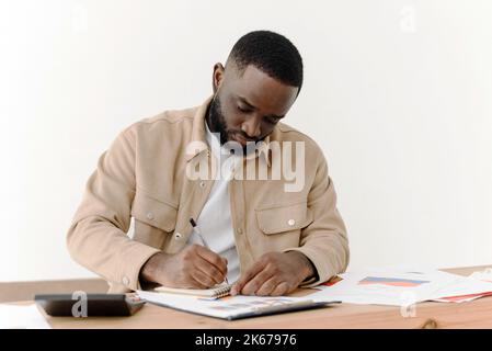Serious african american man reading notes in business paperwork while sitting at home and working on economic project. Stock Photo