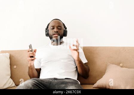 Portrait of an african american young guy enjoying listening to good music at home, sitting on the sofa. Stock Photo