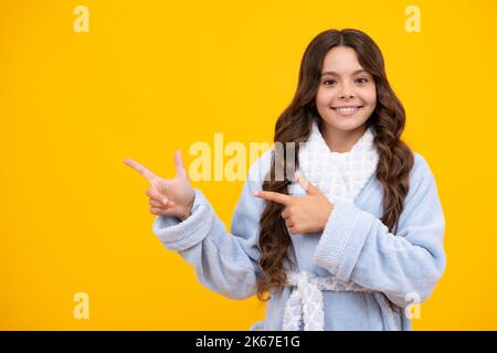 Look at advert. Teenager child points aside shows blank copy space for text promo idea presentation, poses against yellow background. Stock Photo