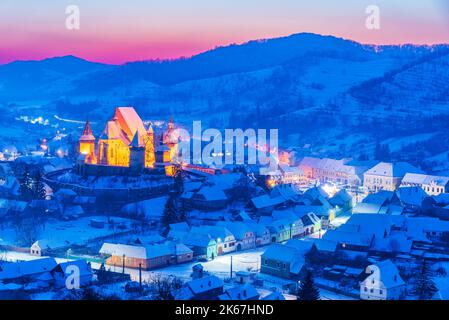 Biertan, Romania. Colored sunset winter rural winter landscape in Transylvania with famous saxon church, travel background in Eastern Europe. Stock Photo