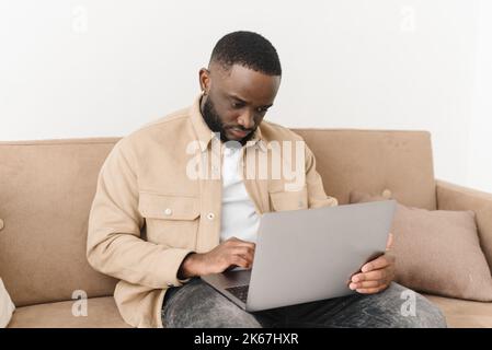 Concentrated young black man shopping online while sitting on sofa at home. African American freelancer working from home Stock Photo