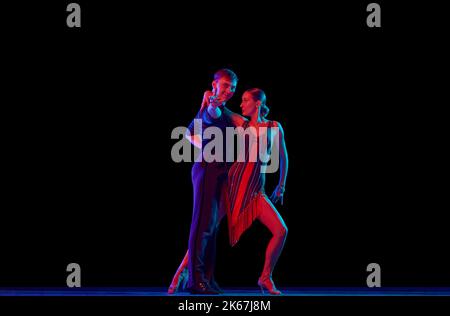 Two dancing people, ballroom dancers in elegance outfits in motion, action over dark background in neon light. Concept of art, music, dance, emotions. Stock Photo